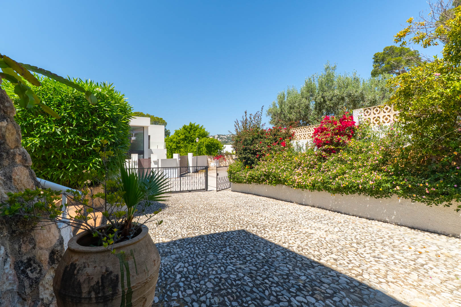 Pebble stone driveway with lush greenery and wrought iron gate.