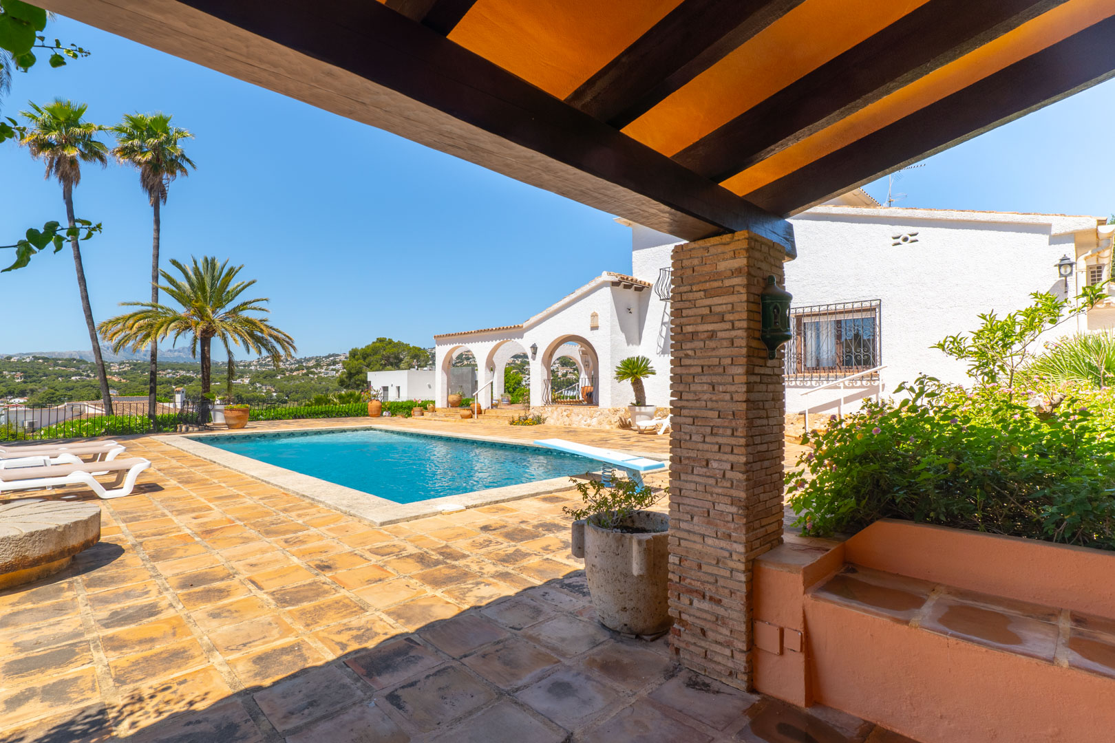 Pool view from covered terrace featuring wooden beams and brick pillars.