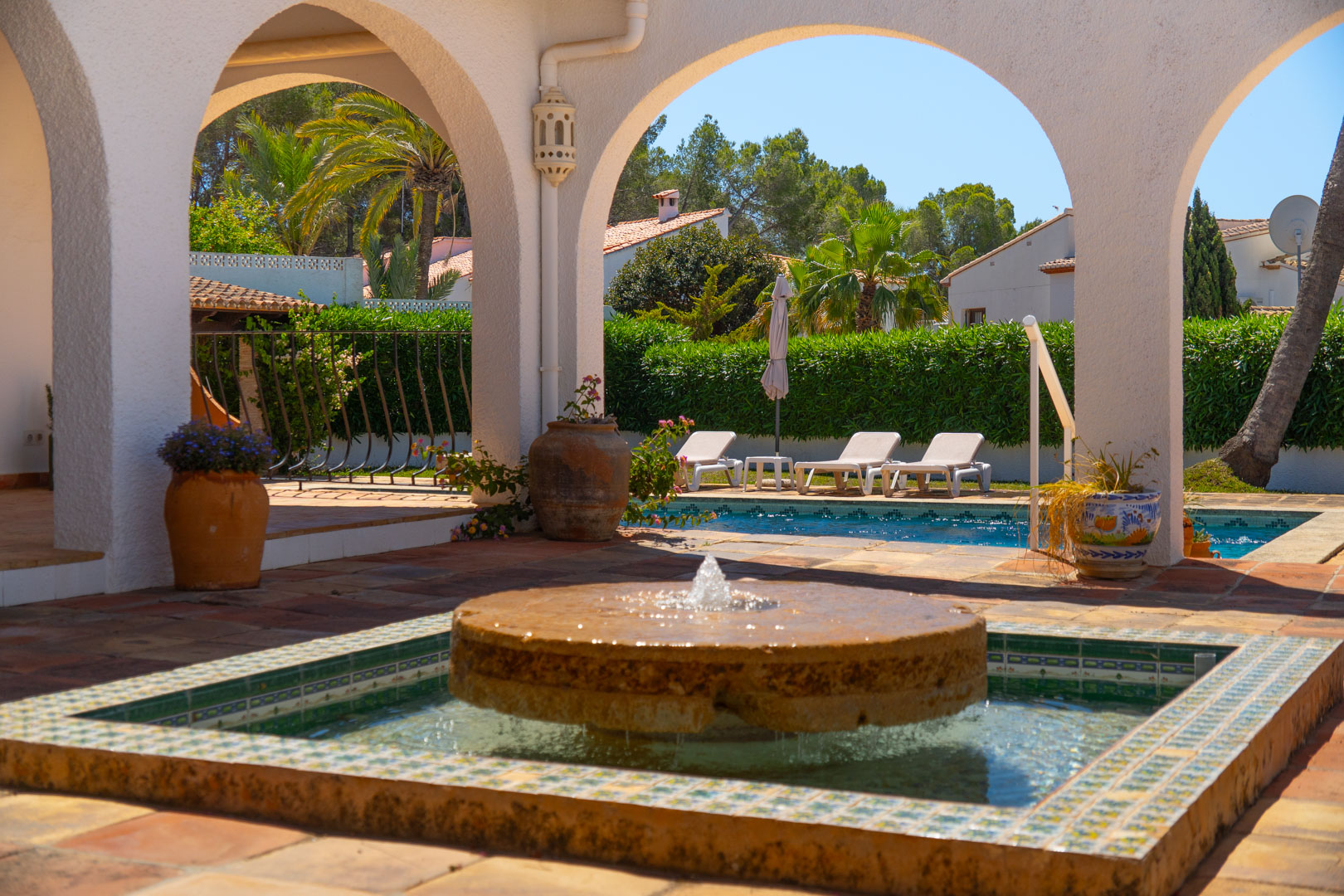 Stone fountain with mosaic tile detail on arched patio and pool.
