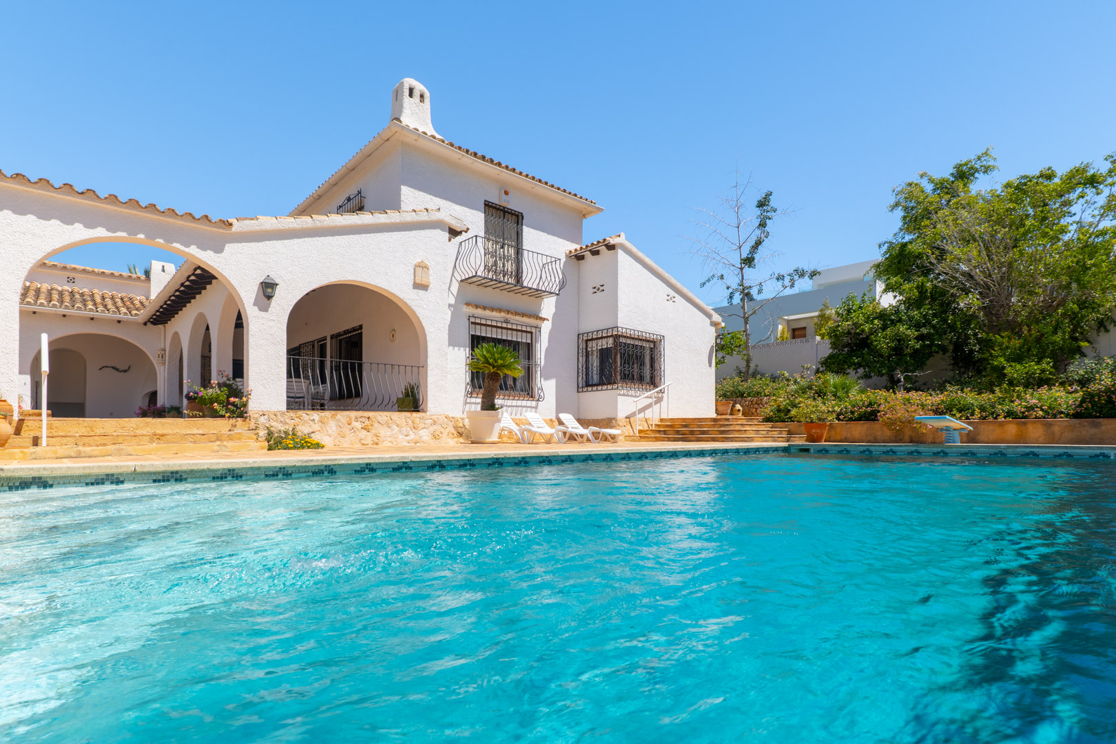 Turquoise pool with mosaic tile edge in front of the white facade.