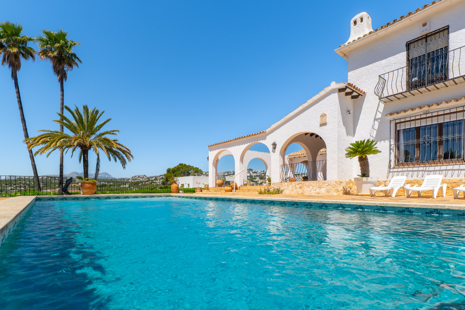 Turquoise pool with mosaic trim and white Mediterranean-style villa with arches.