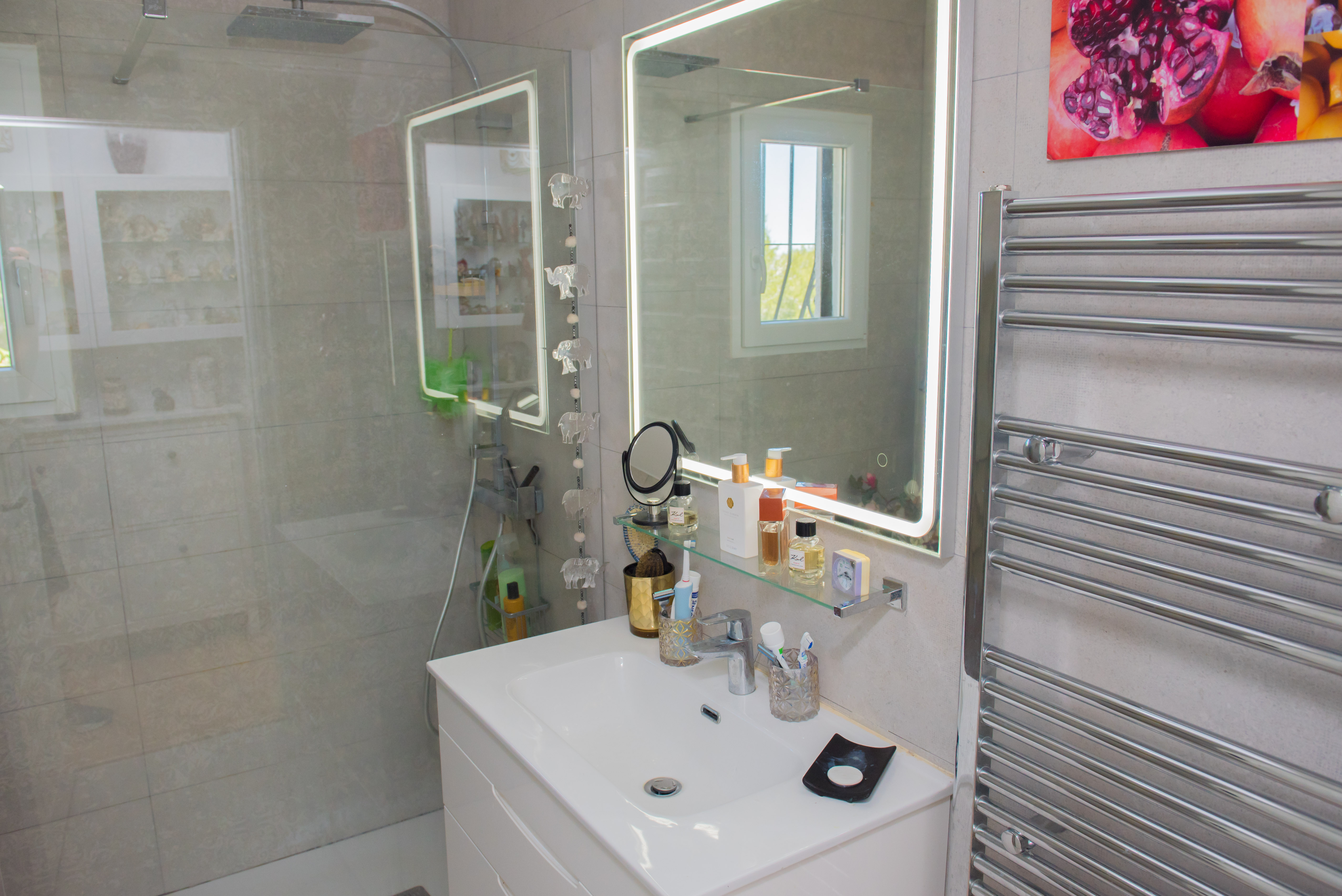 Bathroom detail with white sink, illuminated mirror, and chrome towel warmer.