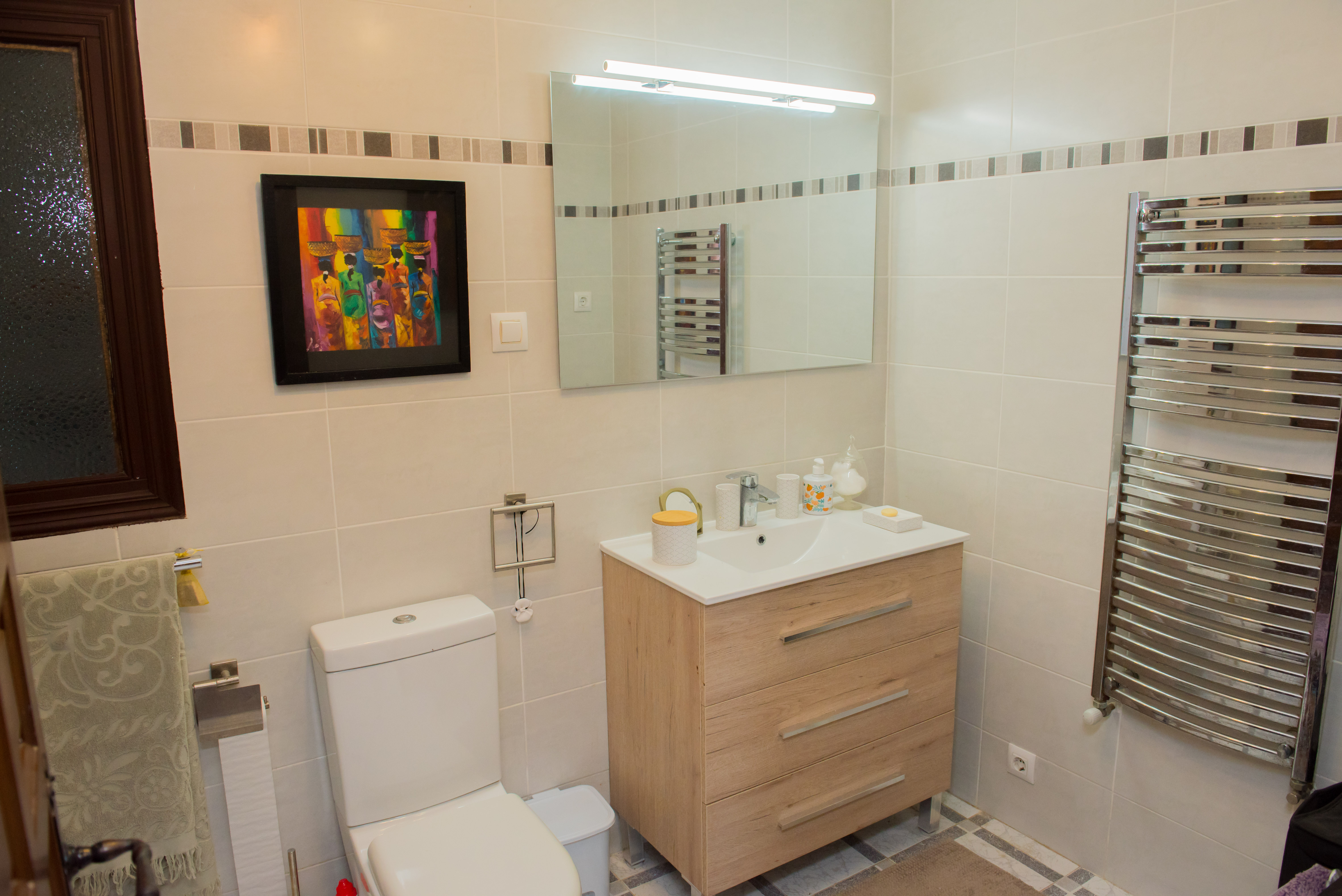 Bathroom featuring cream tiles, light wood vanity, and a chrome heated towel rack.
