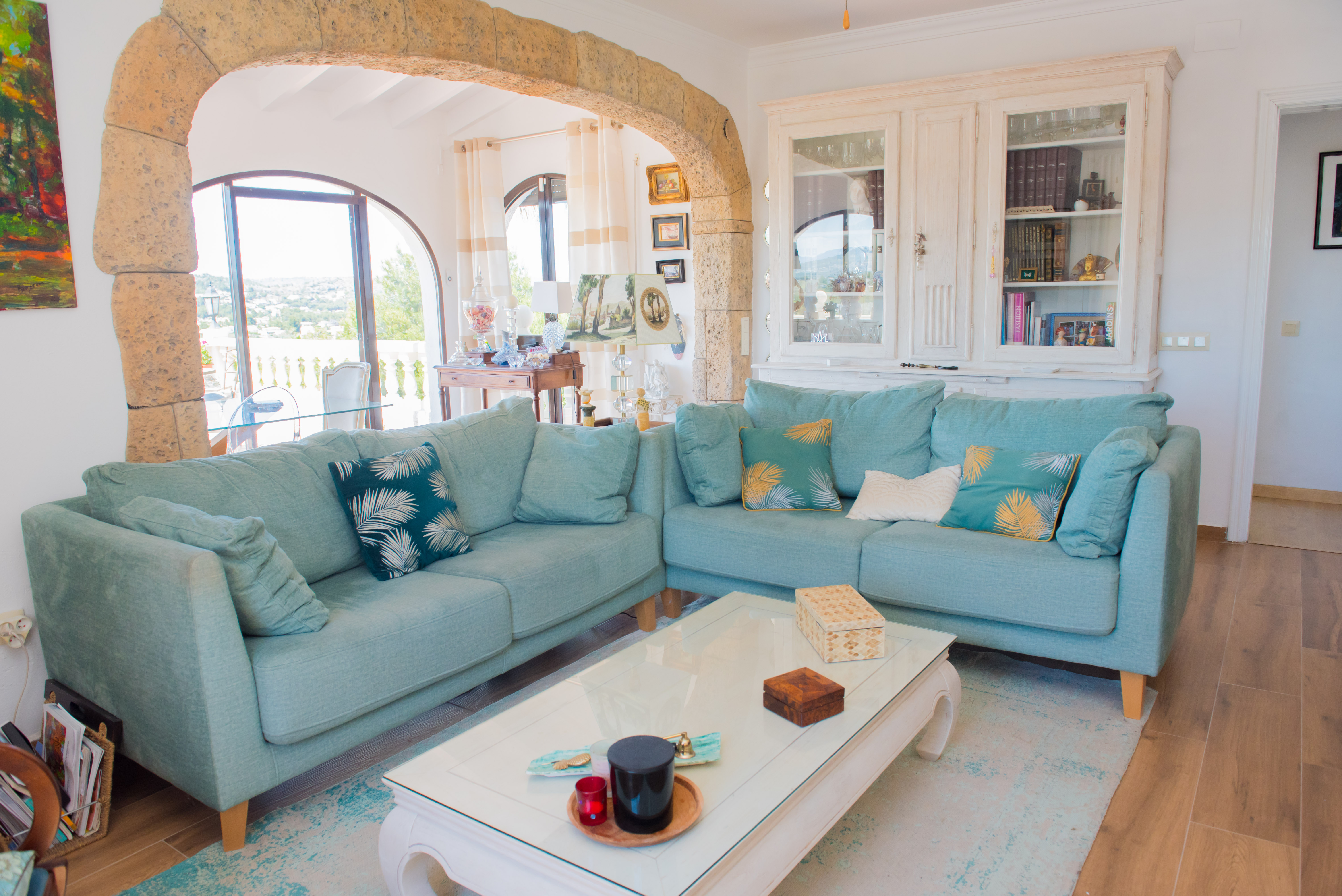 Bright living room with a turquoise sectional sofa, white coffee table, and rustic stone archway framing outdoor views.