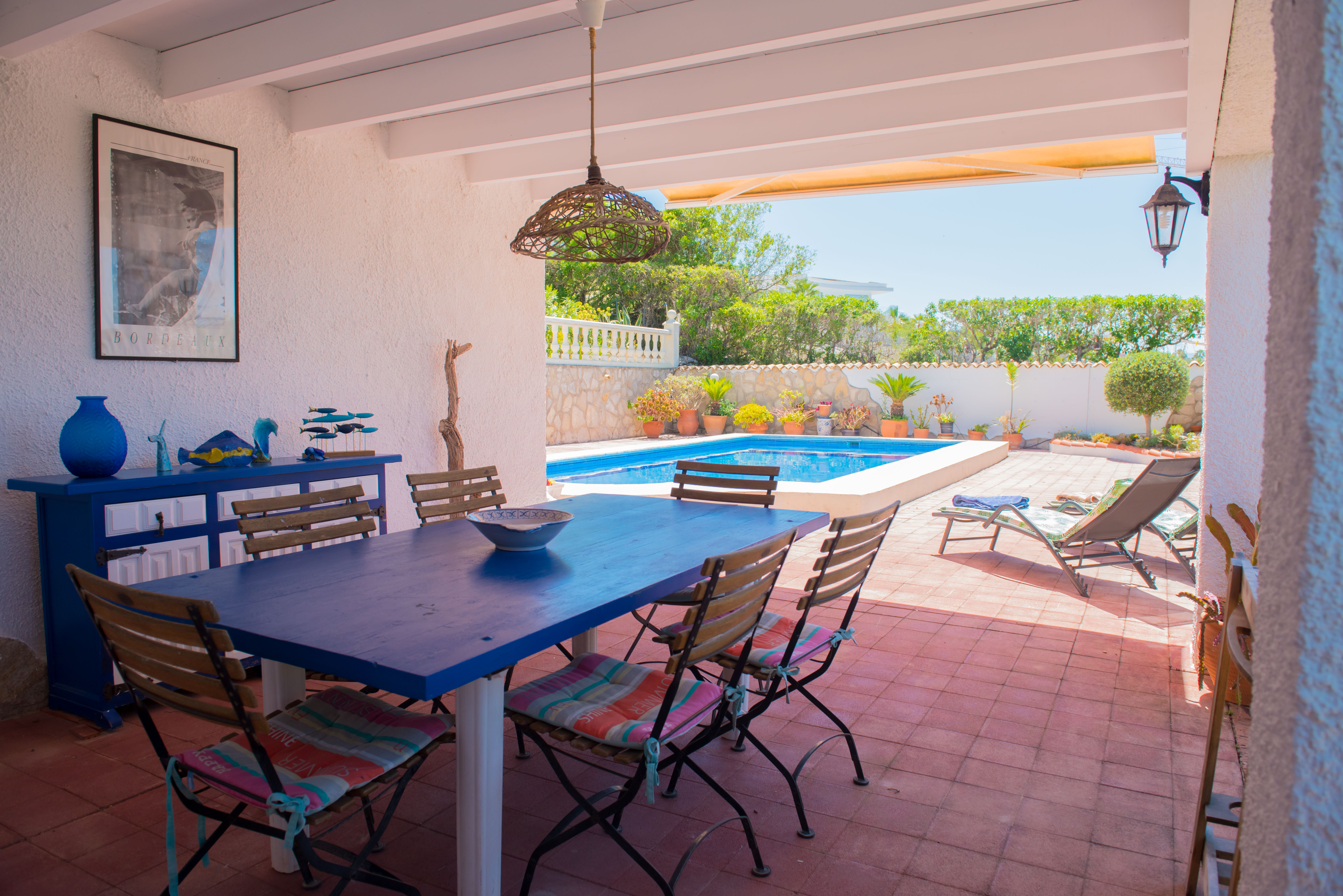 Covered dining area with blue table and pool view.
