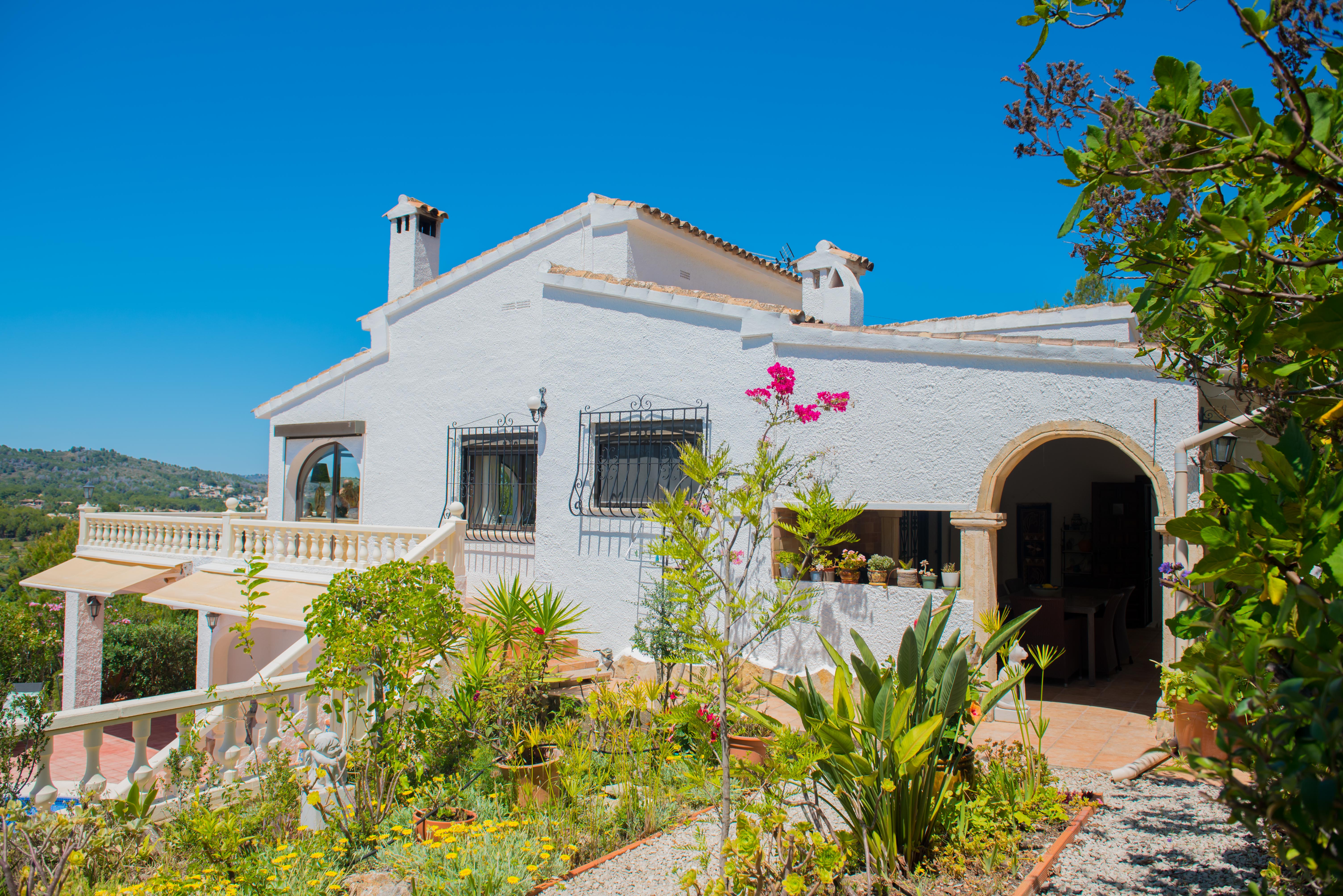 Exterior view of the Mediterranean villa featuring a garden, textured white walls, and balustrade balconies.