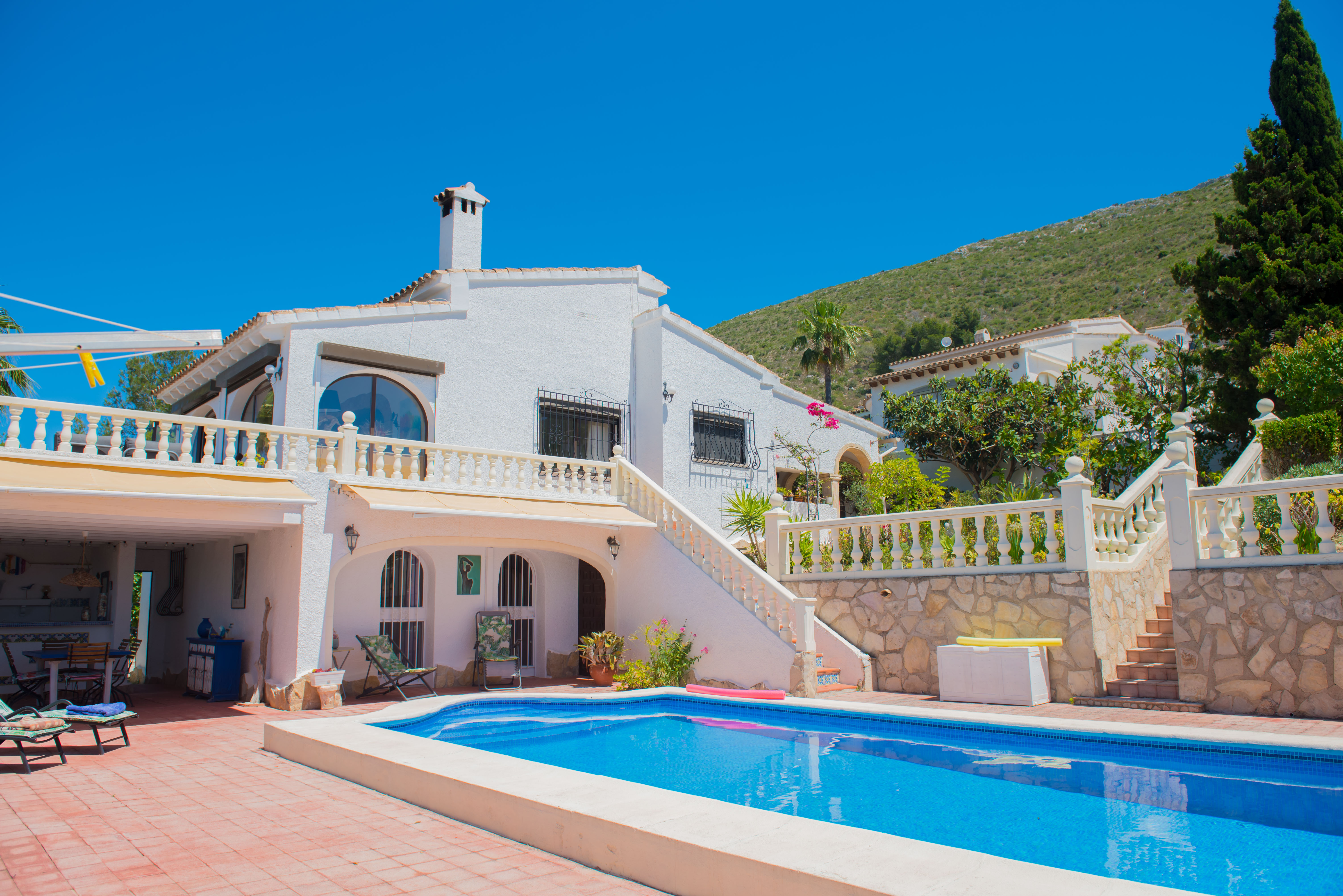 Pool view with red tiling and white Mediterranean-style house with stone staircase.