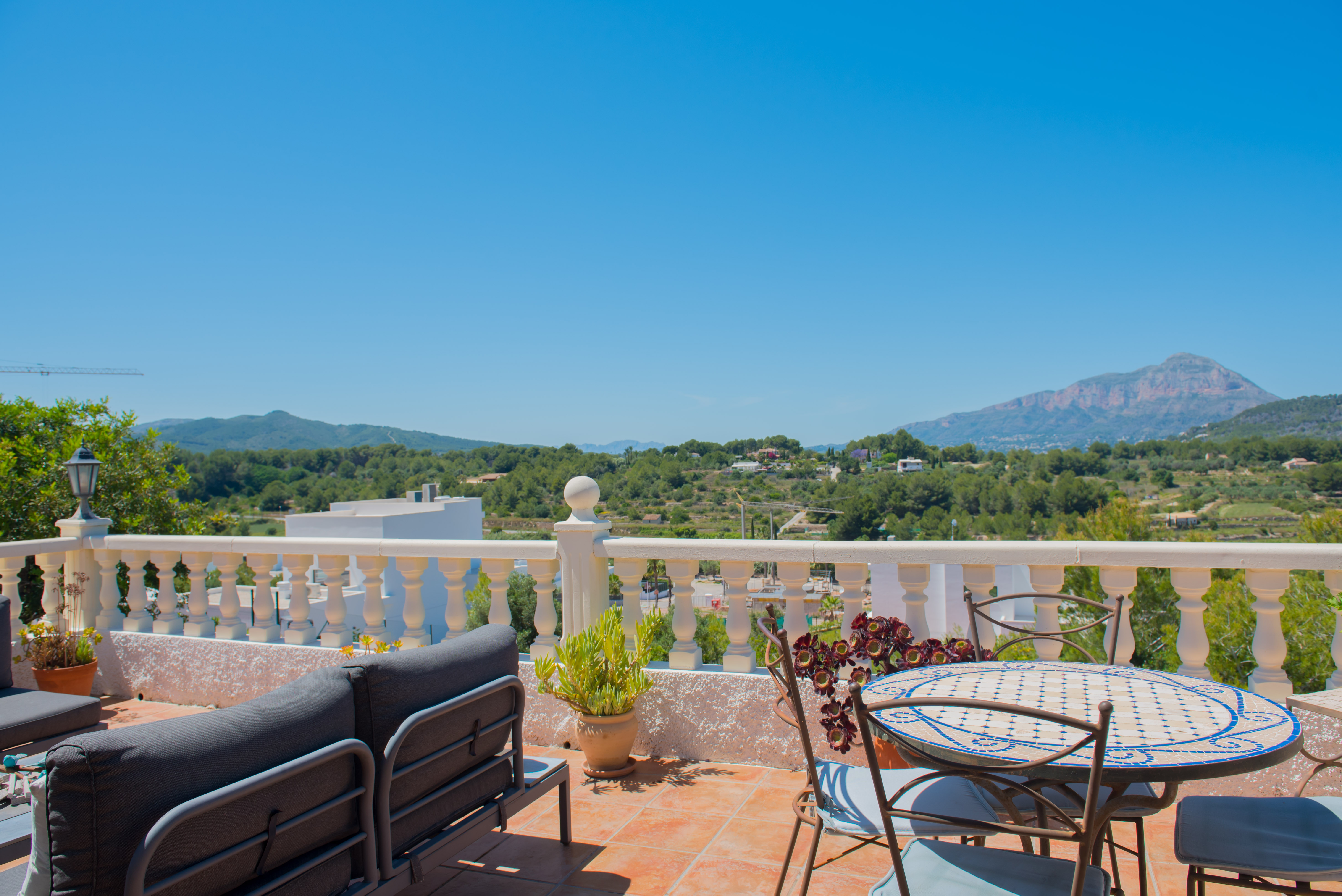 Tiled terrace with mountain views, furnished with a gray sofa and mosaic-topped table.