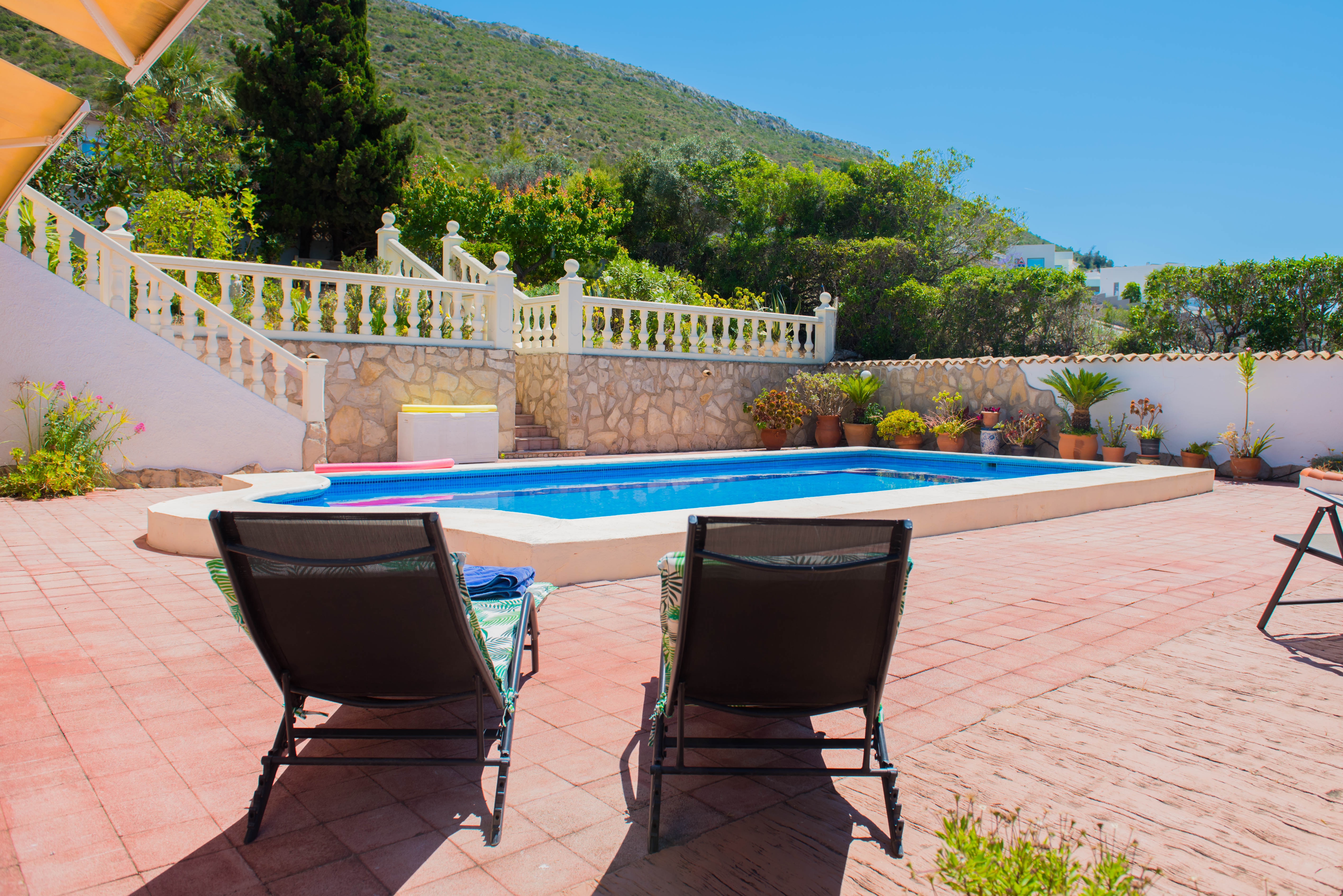 View of the rectangular pool with red tiling and lounge chairs, surrounded by lush greenery.