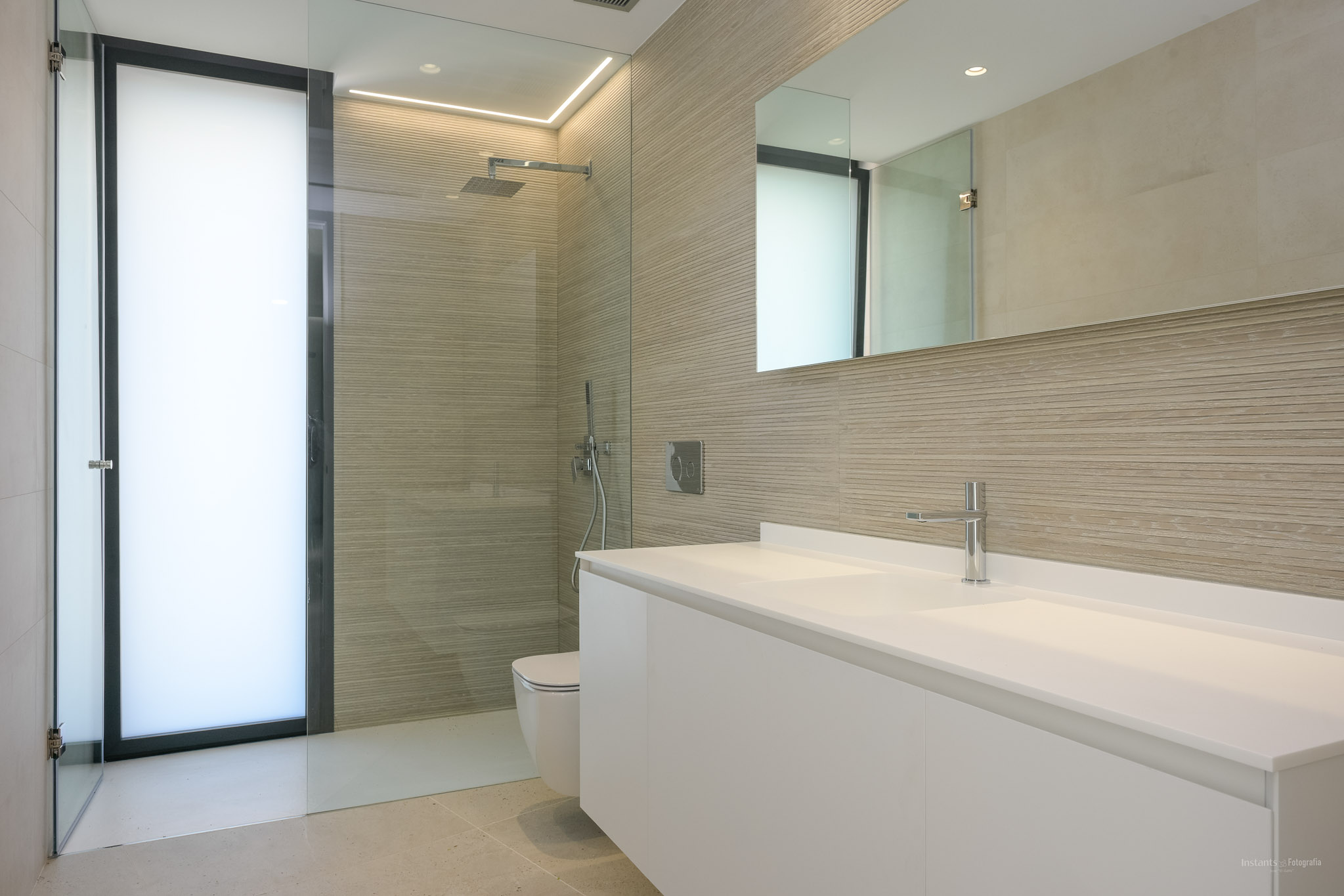 Contemporary bathroom featuring a double white floating vanity, a walk-in shower with textured wall tiles, and a frosted glass door, complemented by modern chrome fixtures and integrated lighting.