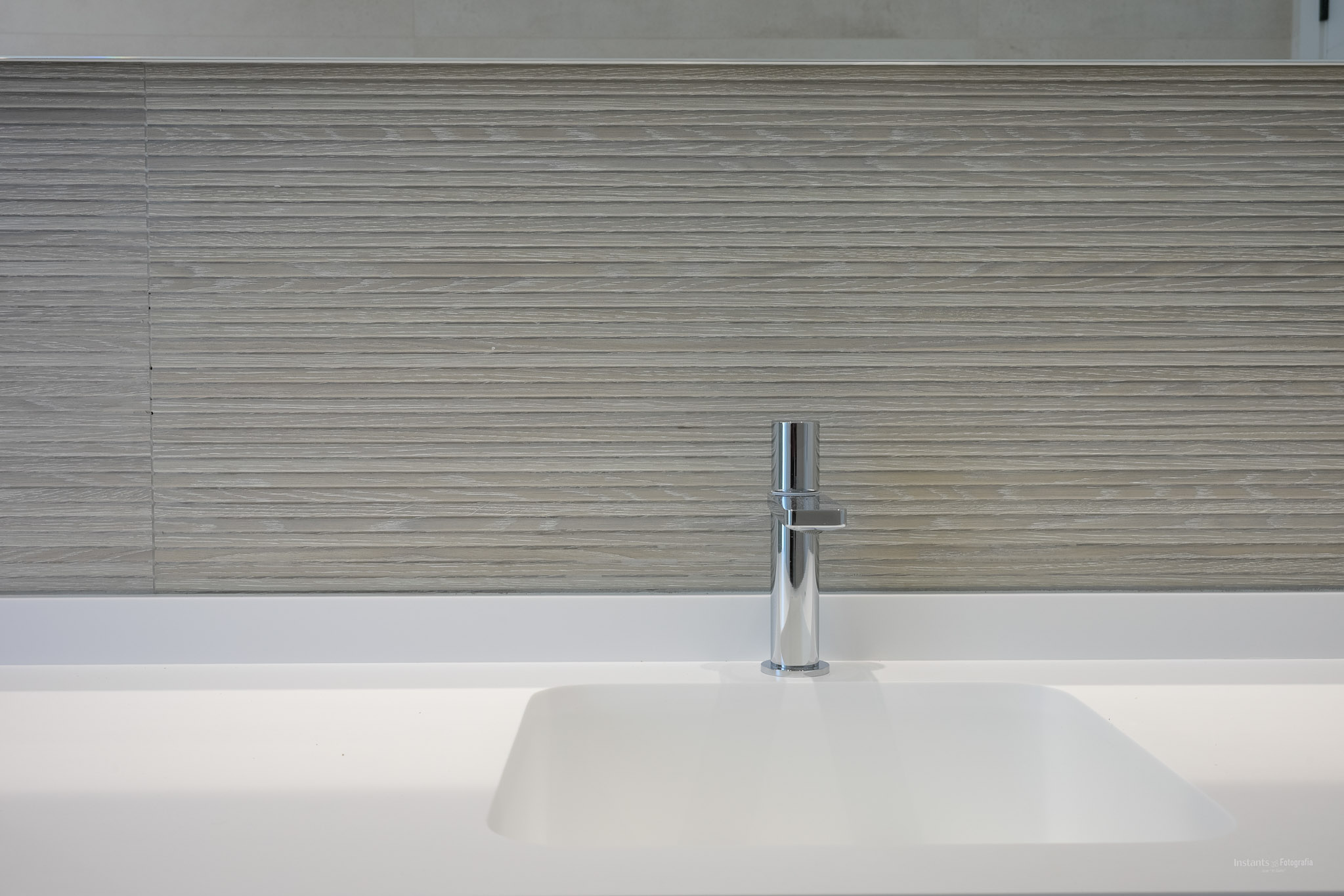 Modern bathroom features an integrated white sink and a sleek chrome faucet. The wall is clad with light-toned, horizontally textured tiles, creating a minimalist yet sophisticated aesthetic.