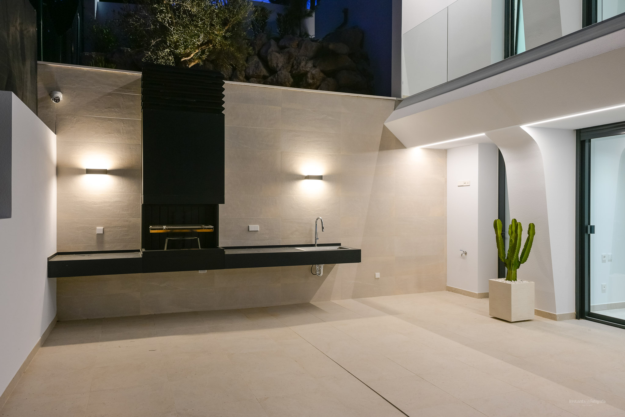 Modern integrated outdoor kitchen with BBQ, stone countertops, and dining area, framed by native vegetation and panoramic Mediterranean sea views.