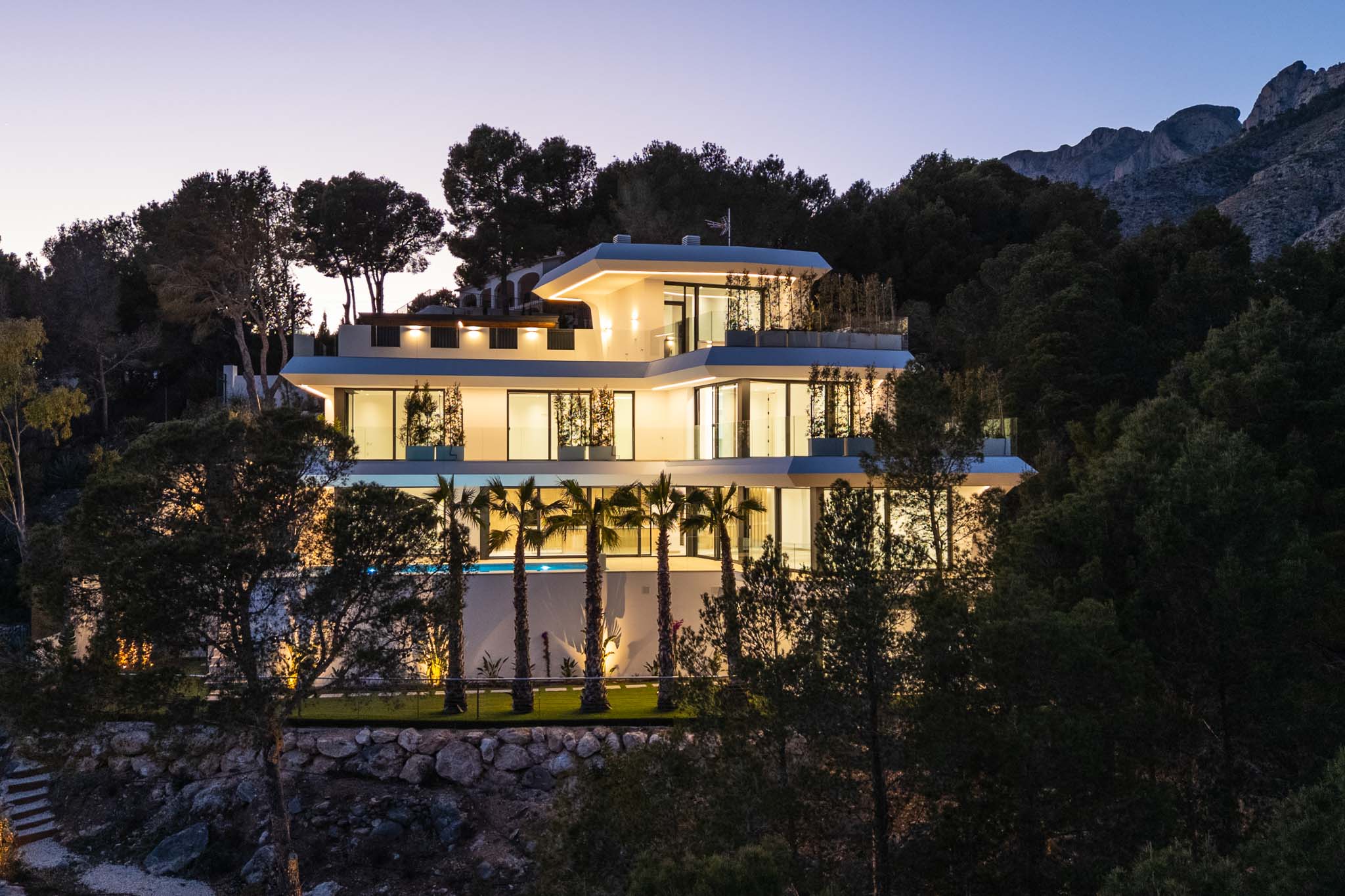 The bright open-plan living room, with light flooring and contemporary furniture, opens through large windows, offering outdoor views and abundant natural light.