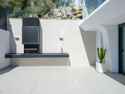 Contemporary outdoor BBQ area featuring an integrated grill and sink, set on light-toned tiled flooring. A potted cactus and natural rock landscaping enhance the space.