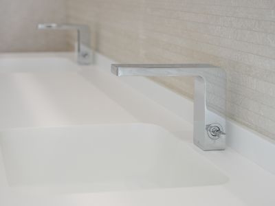 Double vanity featuring sleek chrome faucets and integrated white sinks. The background wall is clad with light, horizontally textured tiles.