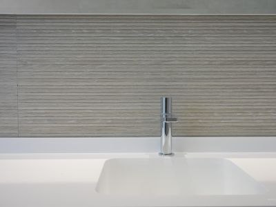 Modern bathroom features an integrated white sink and a sleek chrome faucet. The wall is clad with light-toned, horizontally textured tiles, creating a minimalist yet sophisticated aesthetic.