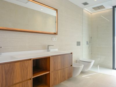 Modern bathroom featuring a double vanity with wooden cabinets, textured wall tiles, and an illuminated mirror. Includes a walk-in shower, wall-mounted toilet, and bidet.