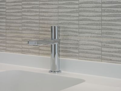 Modern chrome faucet on a white integrated sink countertop, complemented by textured light-colored wall tiles featuring a subtle wave pattern.