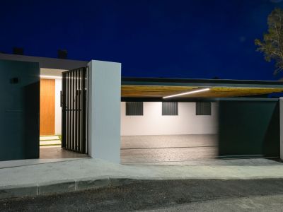 Modern entrance with dark pedestrian gate and wooden main door, alongside an illuminated carport featuring a slatted ceiling and linear LED lighting.
