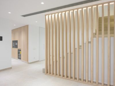 Modern interior featuring a light wood slat partition with integrated lighting, separating a sleek kitchen area with built-in appliances from a contemporary staircase with stone steps.