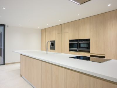 Modern kitchen featuring a large white island with integrated sink and induction hob, complemented by floor-to-ceiling light wood cabinetry and built-in ovens.