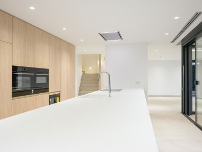 Modern kitchen featuring a long white island with an integrated sink and chrome faucet, complemented by light wood floor-to-ceiling cabinetry and built-in double ovens. Recessed lighting illuminates the contemporary space.