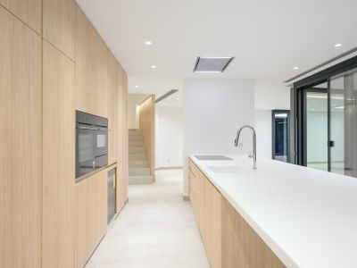 Modern kitchen featuring light wood cabinetry, white countertops, and integrated appliances including an oven, induction hob, and sink with a chrome faucet. Connects to a staircase and outdoor access.