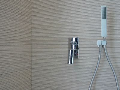 Shower area featuring chrome mixer and handheld shower against a wall clad with horizontally grooved textured tiles.