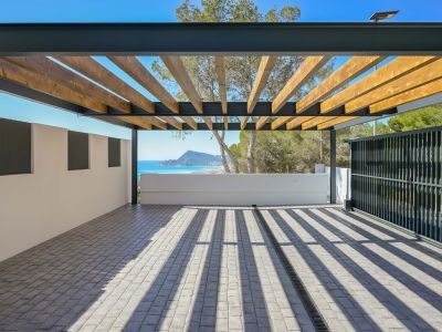 Spacious outdoor area featuring a pergola with wooden beams and a metal frame over cobblestone paving. Enjoy panoramic sea and mountain views, with natural light casting distinct shadows.