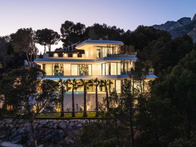 The bright open-plan living room, with light flooring and contemporary furniture, opens through large windows, offering outdoor views and abundant natural light.
