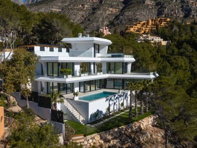 This multi-level contemporary villa features a pristine rectangular pool and expansive terraces with glass railings, nestled into a verdant hillside with mountain views.