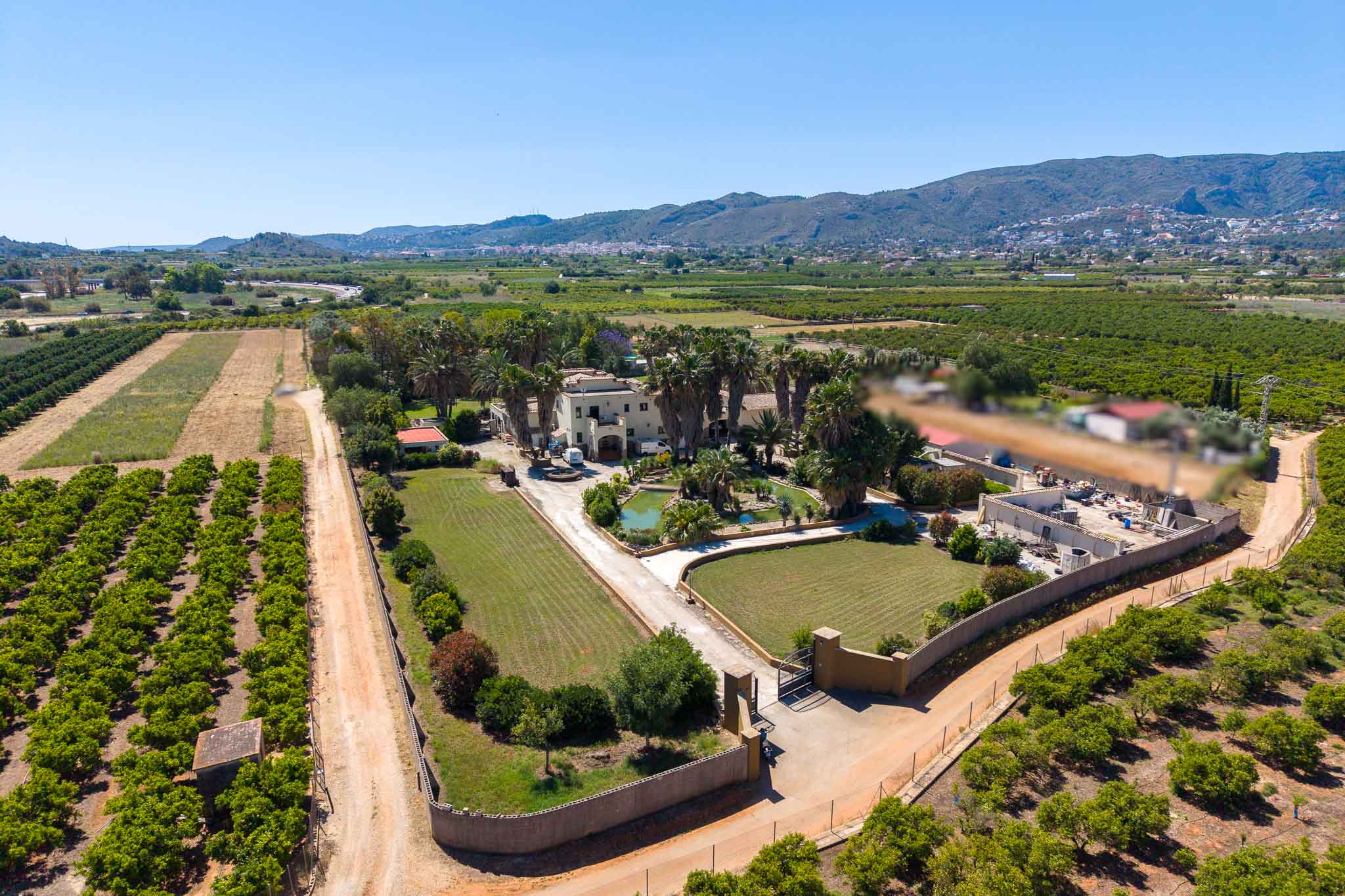 Aerial view of the estate featuring the main house, extensive palm-lined gardens with a pond, surrounded by vast orange groves and distant mountains.