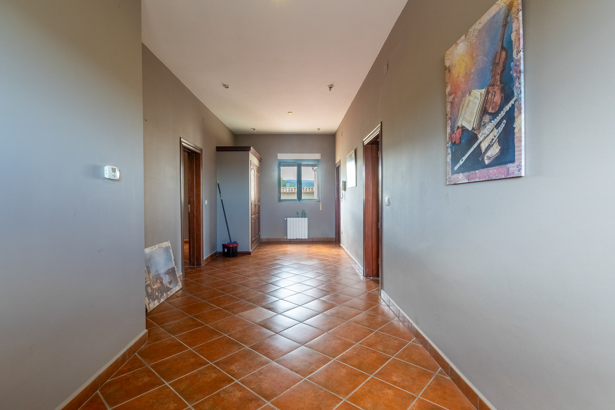Corridor featuring terracotta tiled floors, grey walls, and dark wood doors. A window at the end provides mountain views above a radiator.