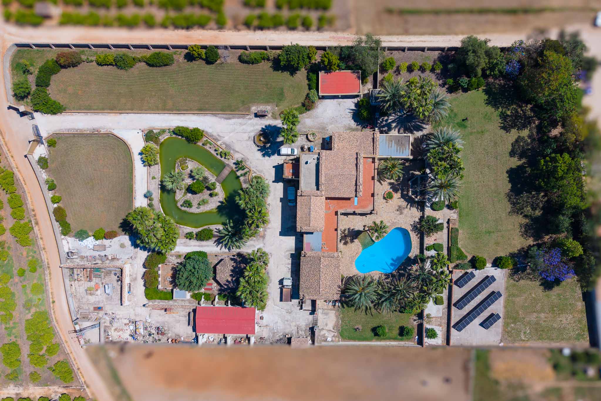 Detailed aerial view of the expansive plot, showcasing the main villa, blue swimming pool, pond with island, and solar panel installation.