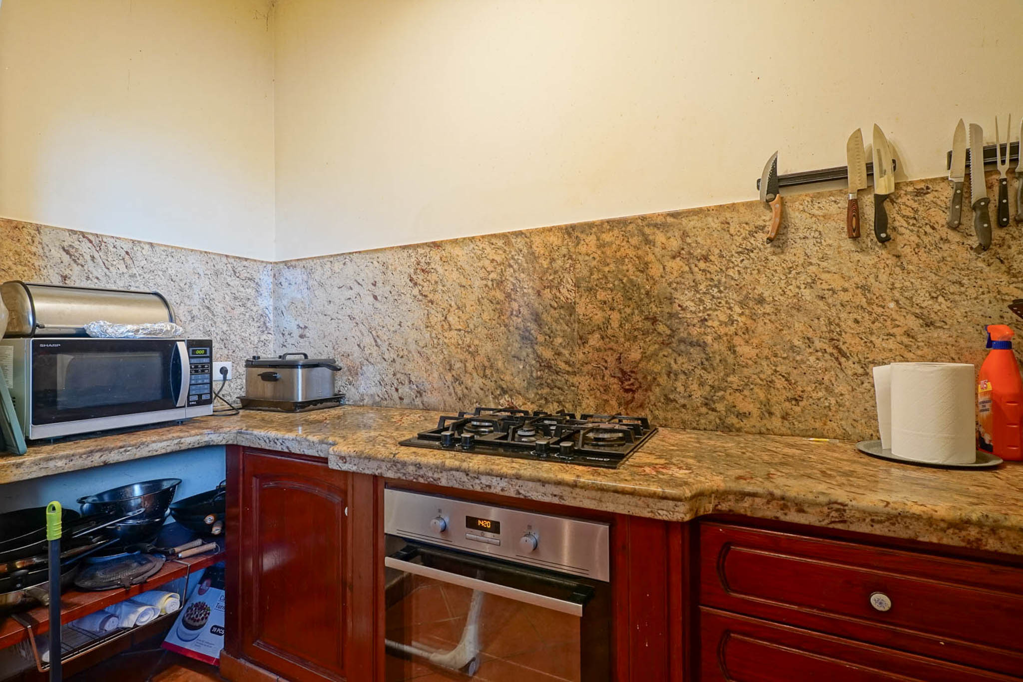 Equipped kitchen corner featuring veined granite countertops and backsplash, with a built-in oven, gas hob, and dark wood cabinetry. Open shelving displays kitchenware.