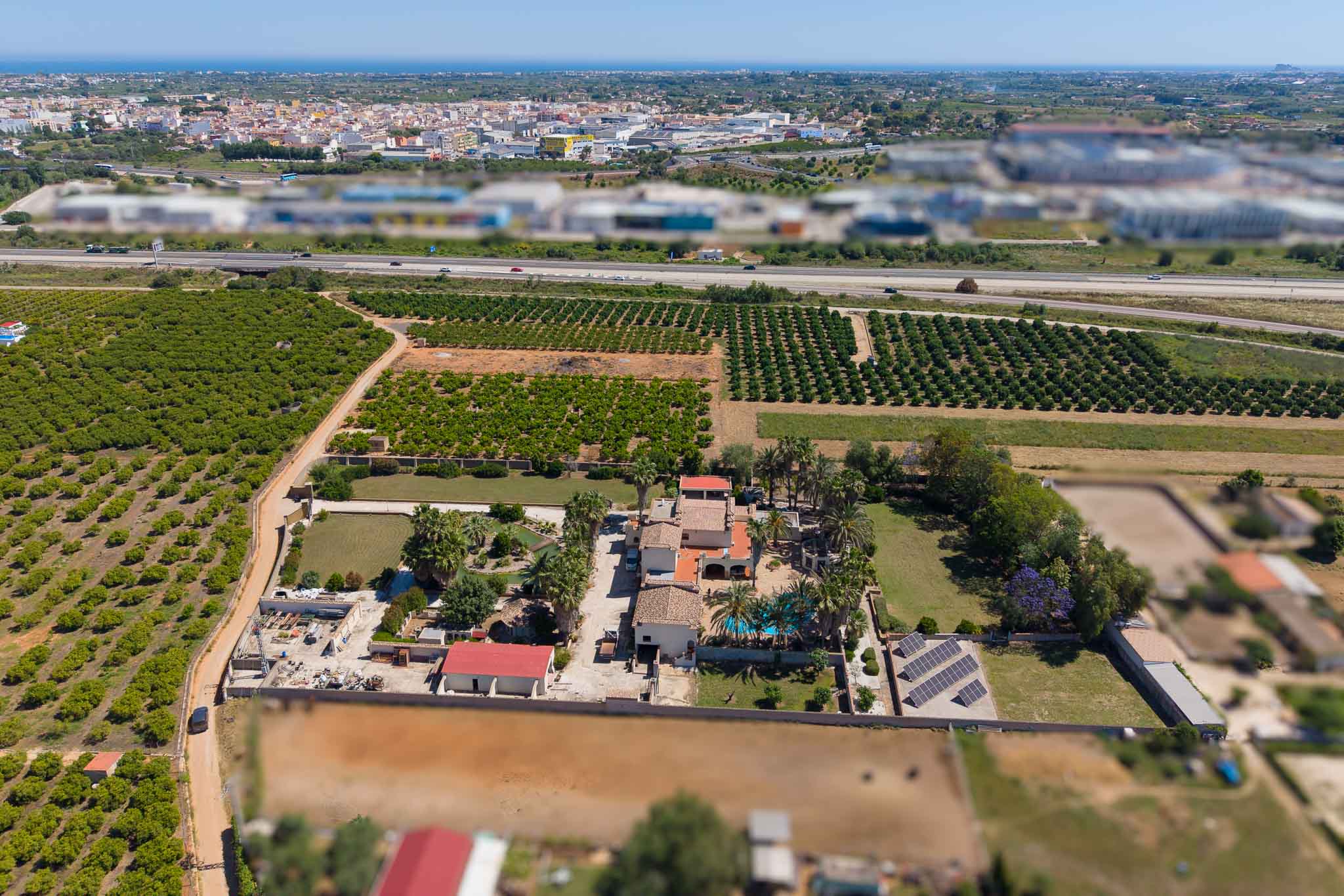 Panoramic aerial view of the property, highlighting its private pool, solar panels, and vast orange groves. A highway, town, and the distant Mediterranean Sea complete the landscape.