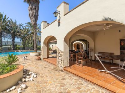 Arched covered terrace with terracotta tiled floor, featuring outdoor furniture and a hammock, adjacent to the swimming pool and palm trees with mountain views.