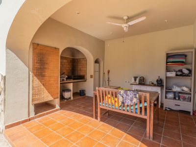 Covered terrace featuring terracotta tiled flooring and a built-in brick barbecue. Includes a wooden dining bench, ceiling fan, and storage, perfect for outdoor entertaining.