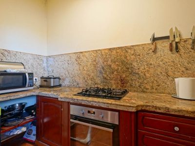 Equipped kitchen corner featuring veined granite countertops and backsplash, with a built-in oven, gas hob, and dark wood cabinetry. Open shelving displays kitchenware.