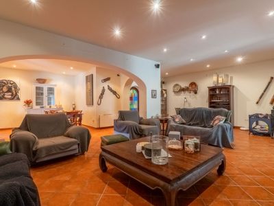 Expansive living room featuring terracotta tiled flooring and recessed ceiling spotlights. Includes a large sofa, armchairs, and a carved wooden coffee table, connecting to a dining area via archways.