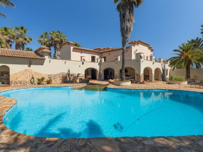 Exterior view of the Mediterranean villa featuring an irregular-shaped private pool with natural stone coping, surrounded by palm trees under a clear blue sky.