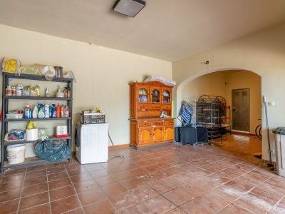 Functional basement utility room with terracotta tiled floor, a washing machine, and extensive shelving for storage, leading to an additional area through an archway.