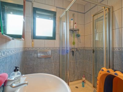 Functional bathroom featuring a ceramic sink, a glass-enclosed shower, and walls tiled in blue and beige. Natural light enters through the window.