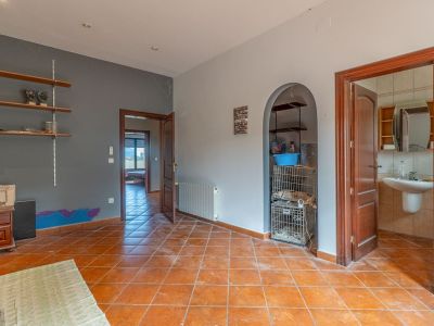 Interior room featuring terracotta floor tiles, two-tone walls, and wooden doors. It includes an arched alcove with shelves and provides access to a bathroom and another room.