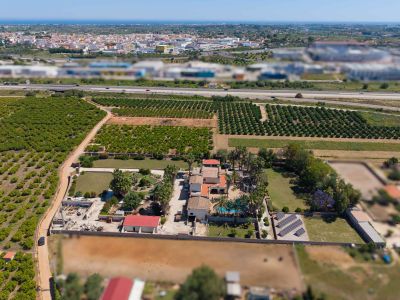 Panoramic aerial view of the property, highlighting its private pool, solar panels, and vast orange groves. A highway, town, and the distant Mediterranean Sea complete the landscape.