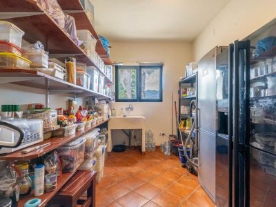 Practical pantry with extensive shelving, a utility sink, and two large refrigerators. Features terracotta tiled floor and a window with palm tree and mountain views.