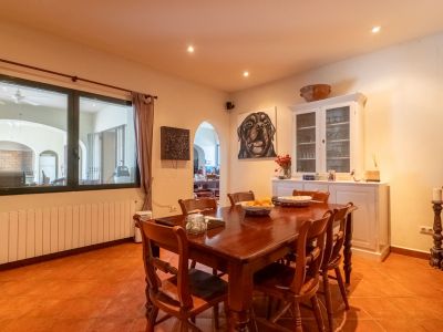 Spacious dining room featuring a dark wooden table and matching chairs, set on terracotta floor tiles. The area includes a radiator below the window and a white display cabinet.