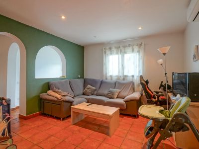 Spacious living area featuring a green accent wall with arched openings, terracotta tiled floor, and a comfortable corner sofa. Includes natural light and a dedicated entertainment zone.