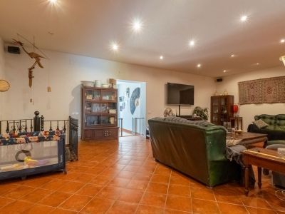 Spacious living area featuring terracotta tiled flooring, recessed ceiling lights, dark leather sofas, and wooden display cabinets. A wall-mounted television and an open archway to a staircase are visible.
