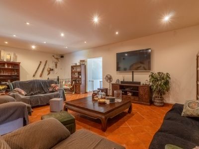 Spacious living room featuring terracotta floor tiles, recessed ceiling spotlights, and a large wall-mounted TV. Furnished with dark wood pieces and covered sofas, creating a warm ambiance.